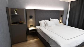 Una habitación de hotel moderna con una cama grande, mesitas de noche, un armario pequeño e iluminación en la pared.