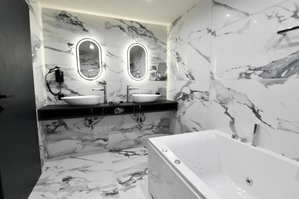 Un baño moderno con paredes de mármol, dos lavamanos y una bañera.