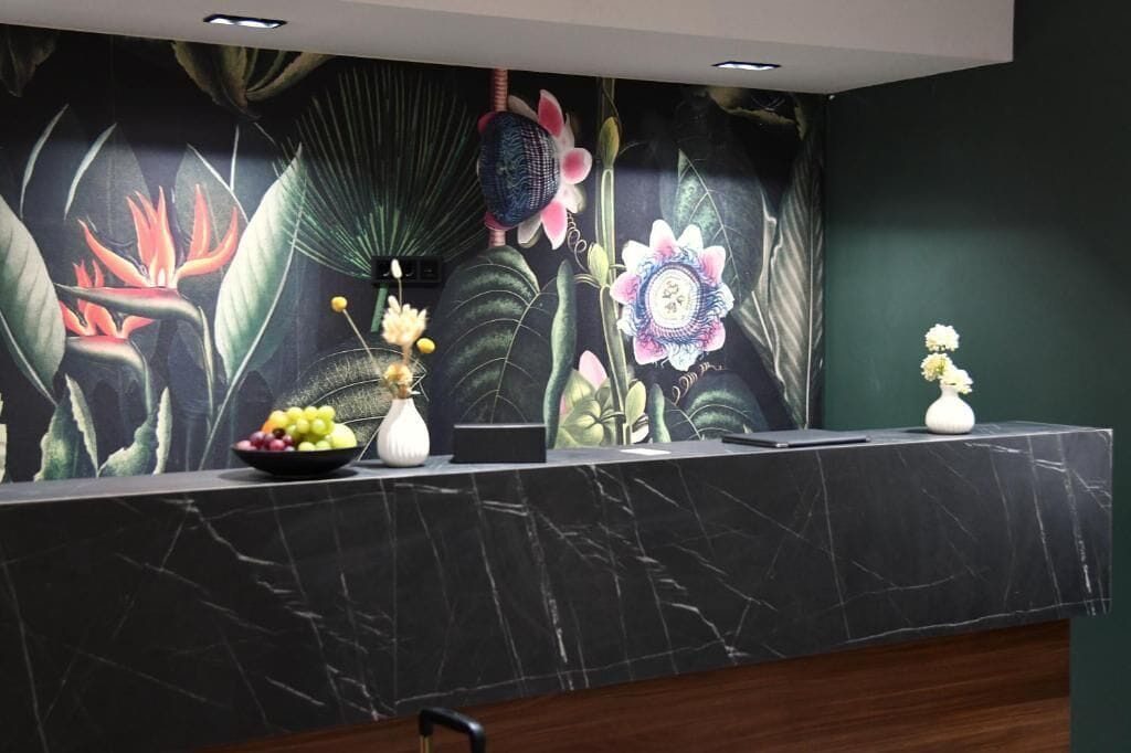 En receptionsdisk med en väggmålning med blommotiv, en skål med frukt och en vas.