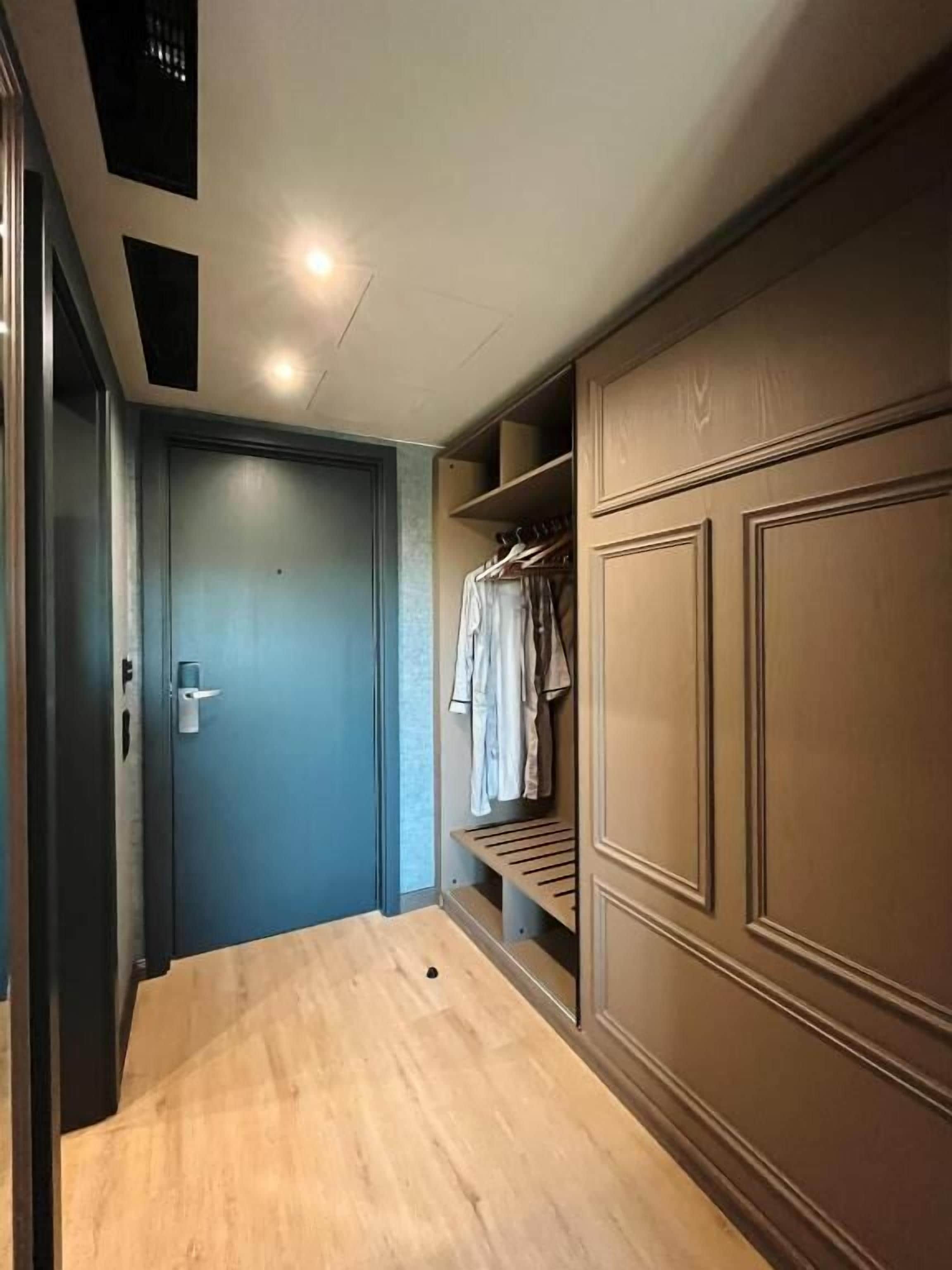 Un pasillo con puerta azul, suelo de madera y armario empotrado con espacio para colgar ropa.