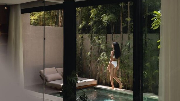A modern indoor pool area with a glass wall, a sofa, and lush greenery visible through the glass.