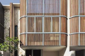 A multi-story building with a modern design, featuring balconies with vertical wooden slats and a stone facade. - VOX Villas Canggu (Bali)