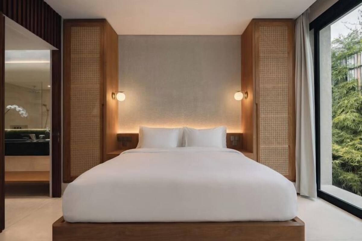 Een moderne hotelkamer met een groot bed, een houten hoofdeinde en uitzicht op groen door het raam.