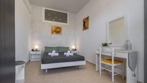 A bedroom with a bed, bedside tables, a desk with a chair, a mirror, and artwork on the walls. - Ranias House Faliraki (Rhodes)