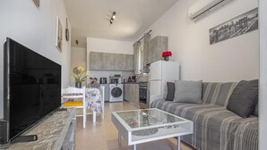 A modern living room with a flat-screen TV, a glass coffee table, a sofa, and a kitchen in the background. - Ranias House Faliraki (Rhodes)