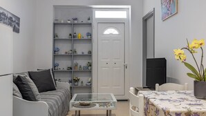 A compact living space with a sofa, a coffee table, a bookshelf, a door, and a television. - Ranias House Faliraki (Rhodes)