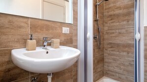 A bathroom with a white sink, a shower with a handheld showerhead, and brown tiled walls. - White star rooms self-check in (Alghero)
