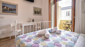 Quarto de hotel com cama, escrivaninha, cadeira e varanda com mesa e cadeiras.