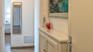 A hallway with a door leading to a room, a framed painting on the wall, and a small decorative item on the console. - White star rooms self-check in (Alghero)