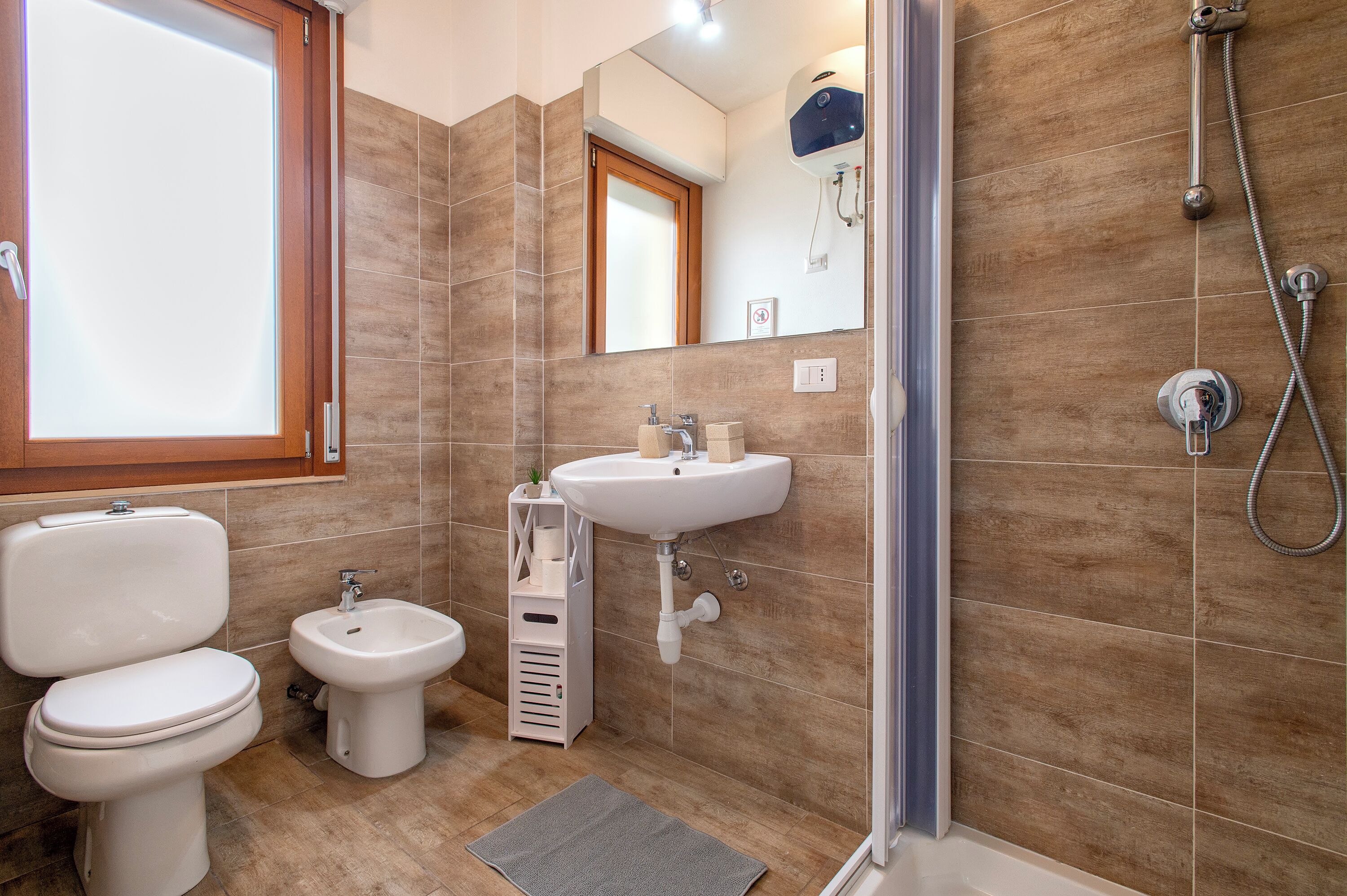 Et badeværelse med toilet, bidet, vask og brusebad.