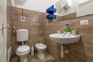 Un baño con inodoro, bidé, lavamanos y espejo.