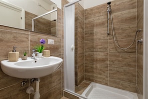 Une salle de bain avec un lavabo blanc, un miroir, une douche avec un pommeau de douche amovible et une baignoire.