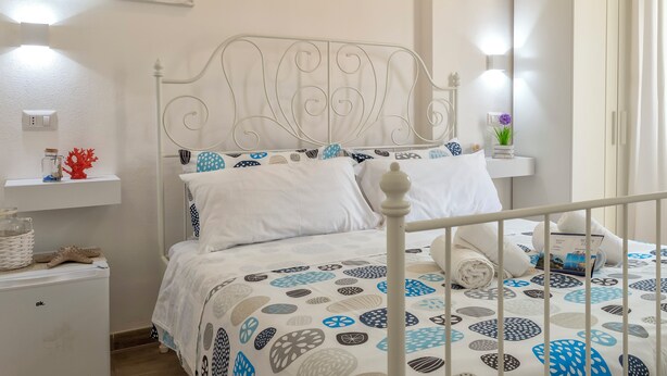 A bedroom with a bed, a nightstand, a wardrobe, and a wall with a framed picture. - White star rooms self-check in (Alghero)