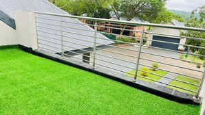 A rooftop with artificial green grass, a metal railing, and a view of a residential area with houses and trees. - The Perazim Place  (Hazyview)