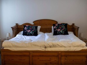 A double bed with a wooden headboard, two black pillows with floral designs, white bedding, and two bedside lamps on wooden nightstands. - 4 Person Holiday Park Home in 82011 (Vallsta)