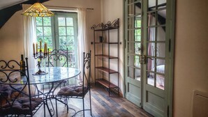 A dining area with a round glass table, cushioned chairs, a candelabra, and a metal shelf unit. - Dordogne gite with pool, terrace and pond, charm & tranquility at Le Pigeonnier (Urval)