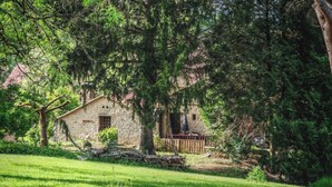 A rustic stone building with a wooden deck, surrounded by lush greenery and trees. - Dordogne gite with pool, terrace and pond, charm & tranquility at Le Pigeonnier (Urval)
