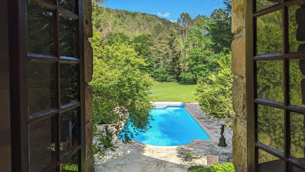 A view of a swimming pool surrounded by a stone patio, with a lush green landscape and trees in the background. - Dordogne gite with pool, terrace and pond, charm & tranquility at Le Pigeonnier (Urval)