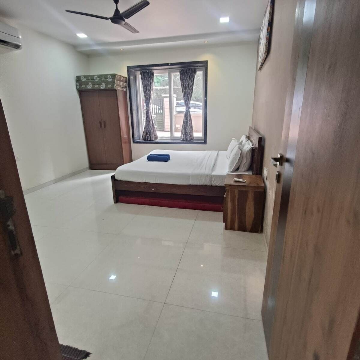 A bedroom with a bed, a wooden nightstand, a wardrobe, a window with curtains, and a ceiling fan.