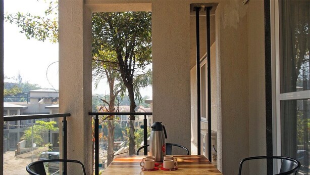 A balcony with a wooden table, two chairs, and a coffee pot. - Mansarovar Bungalows (Lonavala)