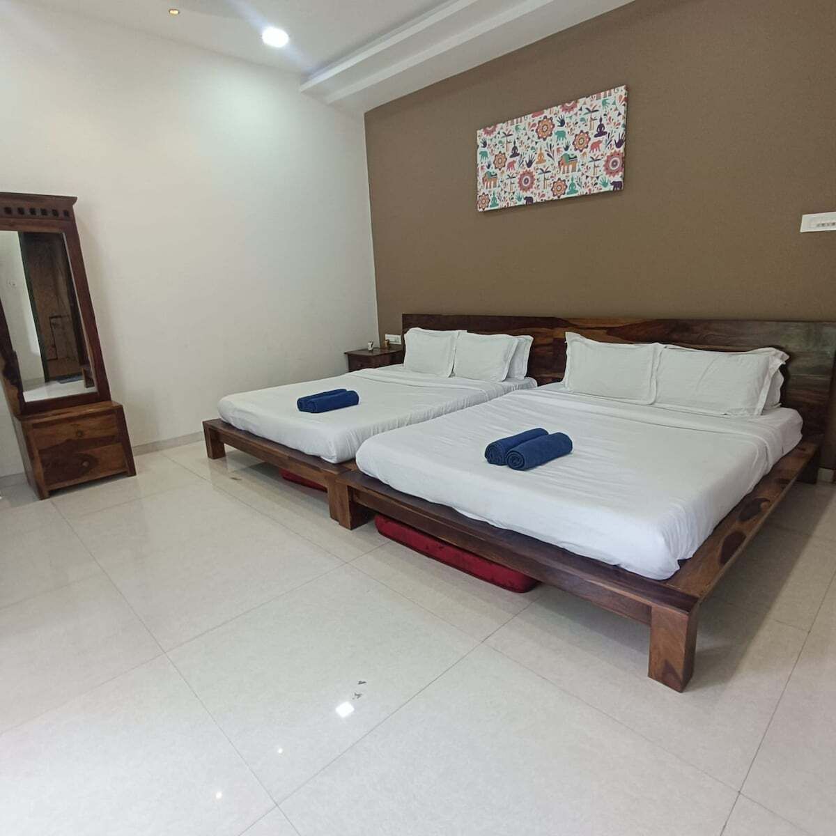 A hotel room with two single beds, a wooden headboard, a large mirror, and a colorful wall decoration.