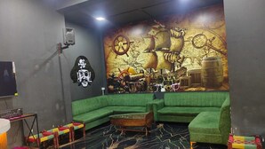 A room with a green sectional sofa, a wooden coffee table, a map mural on the wall, a skull and crossbones decoration, and a flat-screen TV. - Mansarovar Bungalows (Lonavala)