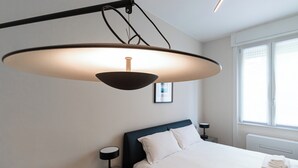 A modern bedroom with a large bed, a bedside table, a hanging light fixture, and a window with blinds. - Italianway Easy - Sebastiano Veniero 27 C - Bilo (Milan)