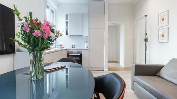 A modern living room with a glass dining table, a grey sofa, and a vase with flowers. - Italianway Easy - Sebastiano Veniero 27 C - Bilo (Milan)