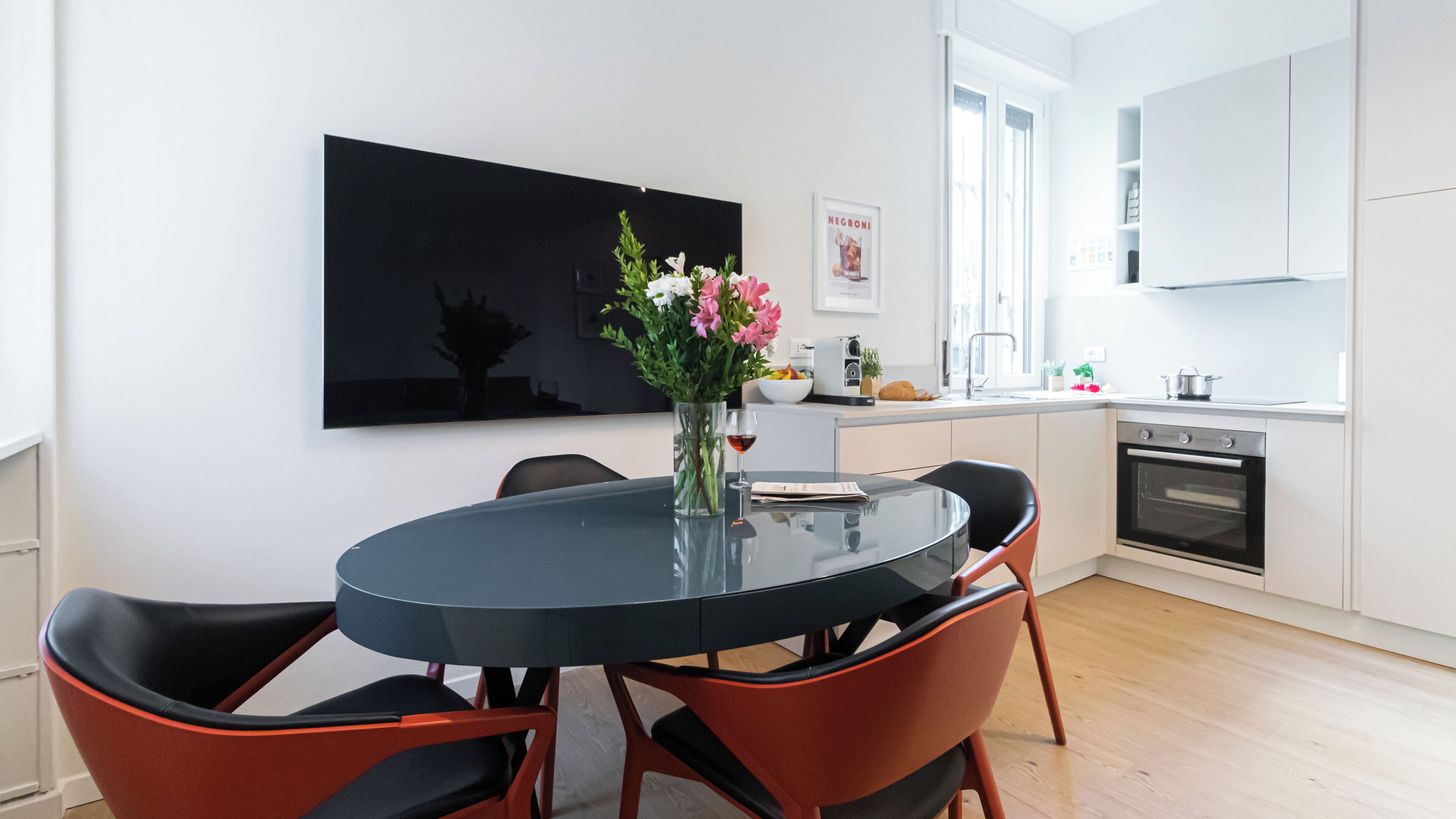 A modern kitchen with white cabinets, a black countertop, and a dining area with a glass table and red chairs.