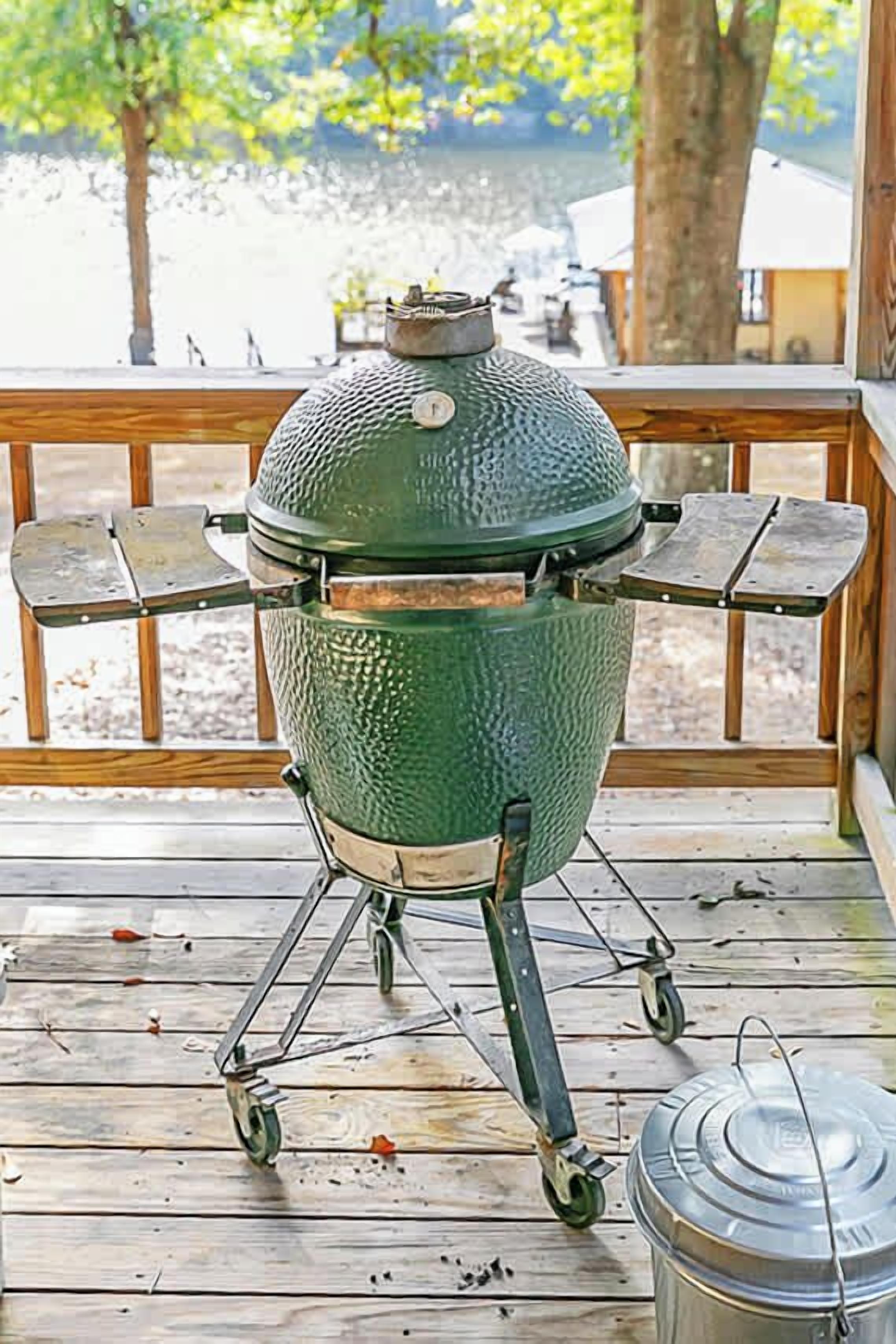 A green barbecue grill on a wooden deck with a view of a lake and trees.