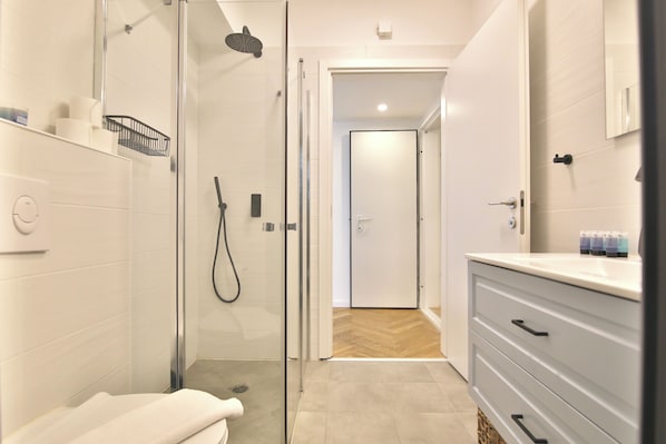 Un baño moderno con cabina de ducha de vidrio, un tocador blanco con cajones y un suelo con estampado de espiga.