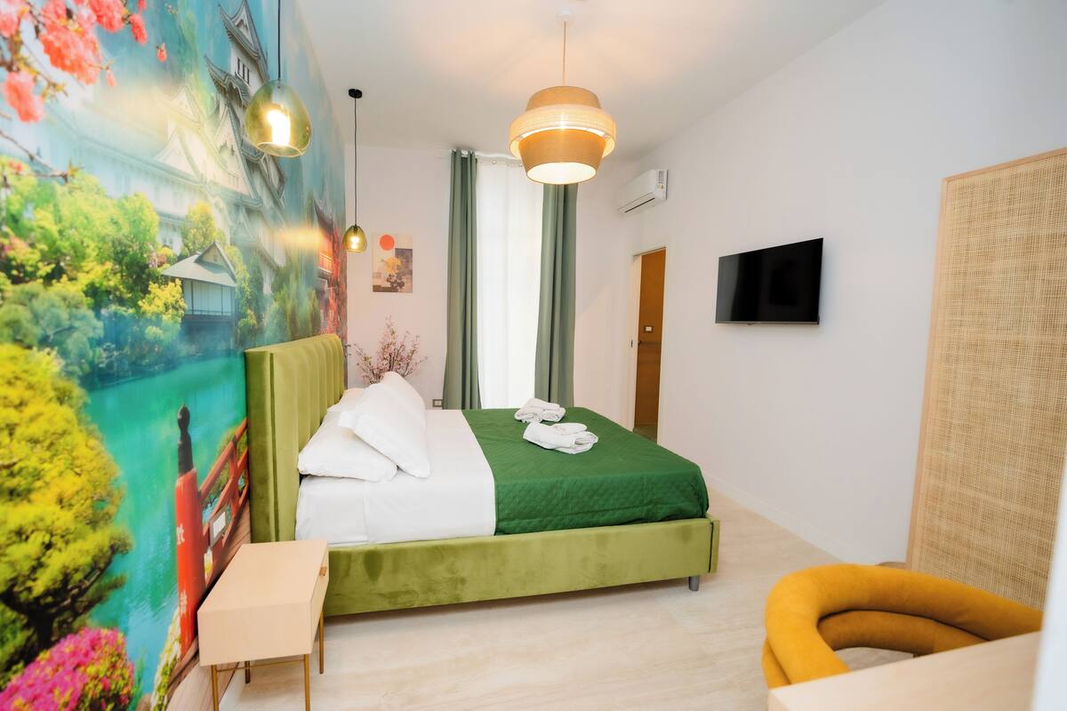 A hotel room with a bed, a television, a painting, and a window with curtains.