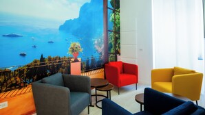 A room with a mural of a coastal scene, a red chair, a yellow chair, and a grey armchair. - Four Points Suites (Naples)