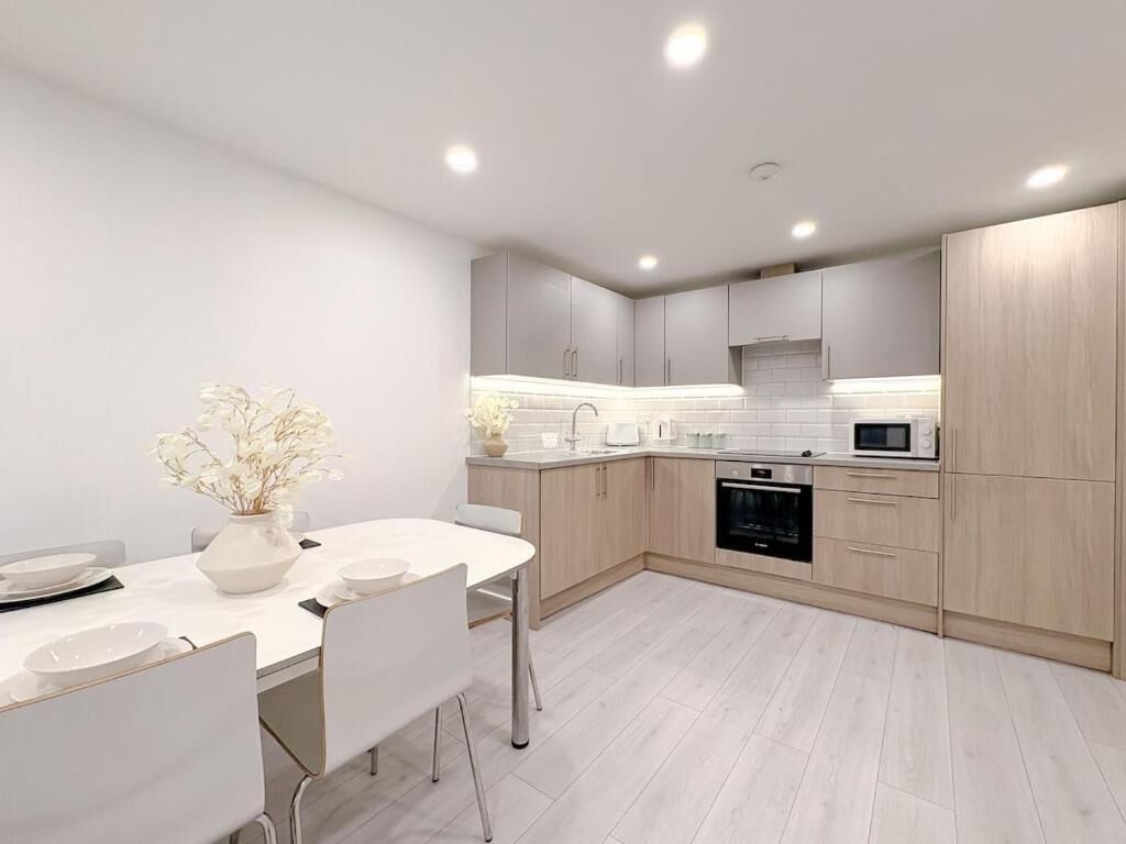 Een moderne keuken met witte kasten, een wit aanrechtblad en een eethoek met een witte tafel en stoelen.