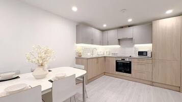 Een moderne keuken met witte kasten, een wit aanrechtblad en een eethoek met een witte tafel en stoelen.