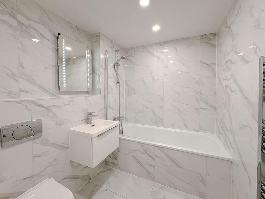 Une salle de bain moderne avec un mur en marbre, un lavabo blanc, un miroir et une baignoire.