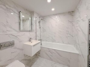 A modern bathroom with a marble wall, a white sink, a mirror, and a bathtub.