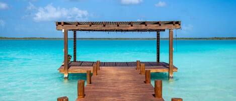 A wooden pier leading to a wooden gazebo over clear turquoise water.