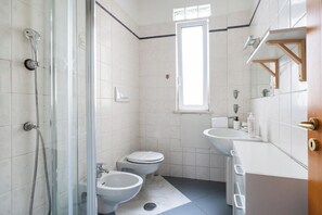 A bathroom with a glass shower enclosure, two toilets, a bidet, a sink, and a window providing natural light. - Lovely Terrace Apartment by Wonderful Italy (Bari)