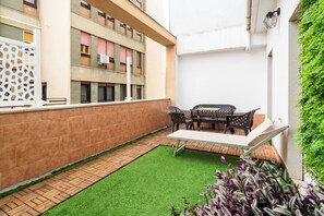 A courtyard with a green lawn, a seating area with chairs and a table, and a white wall with a window. - Lovely Terrace Apartment by Wonderful Italy (Bari)