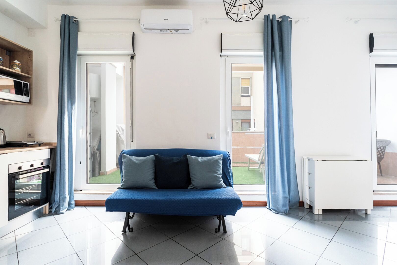 Una sala de estar moderna con un sofá azul, una zona de cocina y un puerta corrediza de vidrio que da a un patio exterior.