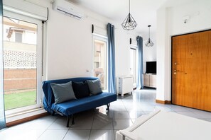 A modern living room with a blue sofa, a TV, and a wooden door. - Lovely Terrace Apartment by Wonderful Italy (Bari)