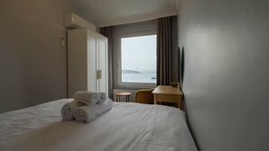 Quarto de hotel com cama, janela vista para o mar, mesa pequena e uma cadeira.