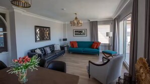 Uma sala de estar moderna com um sofá de couro preto, um sofá verde-água com almofadas laranja, uma mesa de jantar com um vaso de flores e um candelabro.