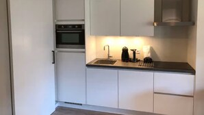 Una cocina moderna con armarios blancos, un horno de acero inoxidable, una cafetera y un lavamanos.