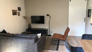 Una sala de estar moderna con un sofá gris, un sillón marrón, un televisor y una mesita.
