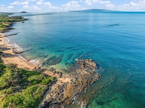 Eine Küstenlandschaft mit klarem, blauem Wasser, einem Sandstrand und felsigem Gelände.