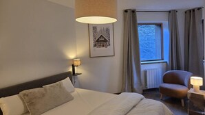A hotel room with a bed, a chair, a lamp, a picture on the wall, and a window with curtains. - Apartment 3R, 6 ppl, Valmorel with Parking (Valmorel)