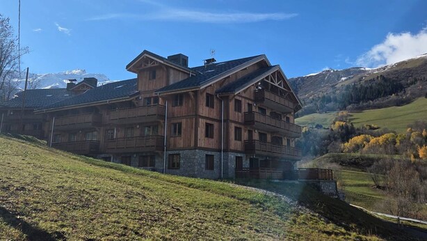 A large wooden chalet with multiple balconies, set against a mountainous backdrop. - Apartment 3R, 6 ppl, Valmorel with Parking (Valmorel)