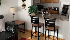 A compact living space with a kitchenette, a dining area with two chairs, a sofa, a small table, and a lamp.